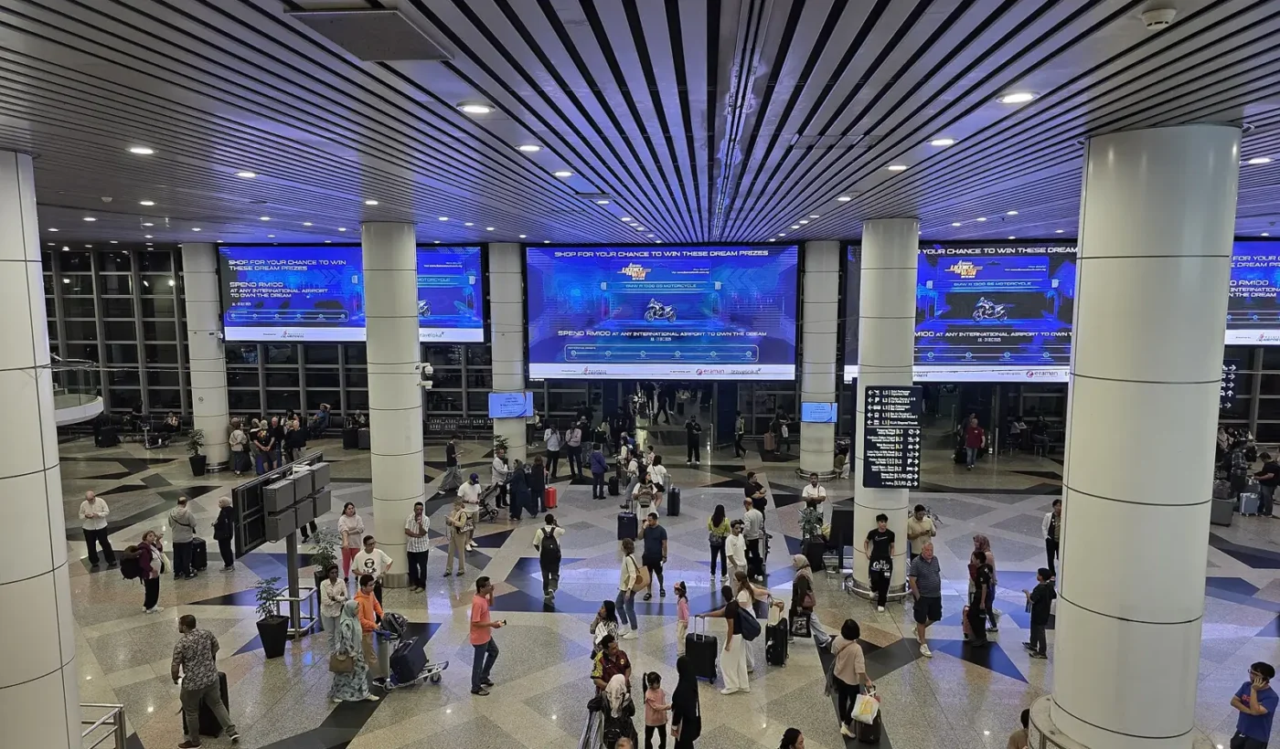 쿠알라룸푸르 국제공항 제1터미널 3층 도착장에서 짐을 끄는 여행자들과 대형 전광판