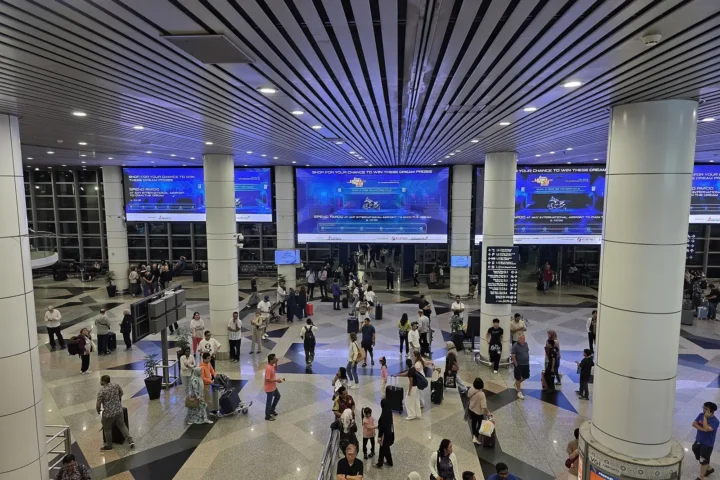 쿠알라룸푸르 국제공항 제1터미널 3층 도착장에서 짐을 끄는 여행자들과 대형 전광판